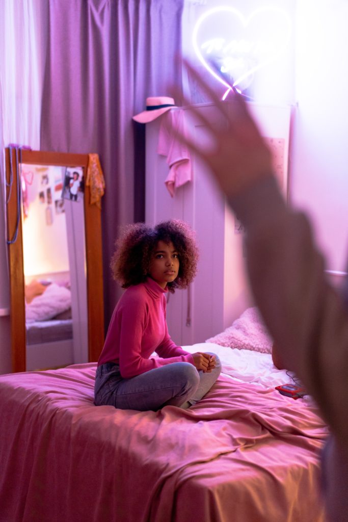 a teen sits on her bed and appears frustrated with an adult standing in her doorway