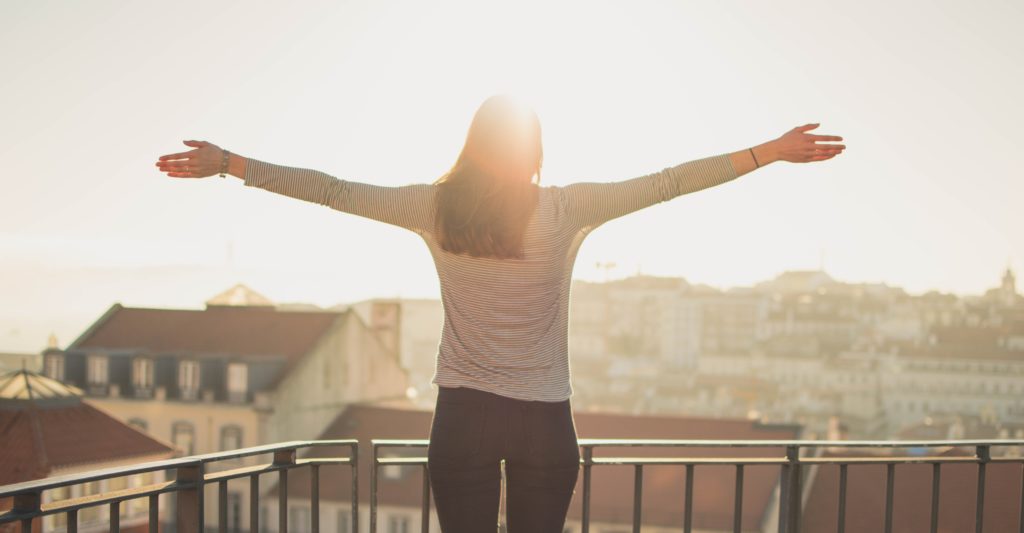 a woman stands with arms open basking in the sun